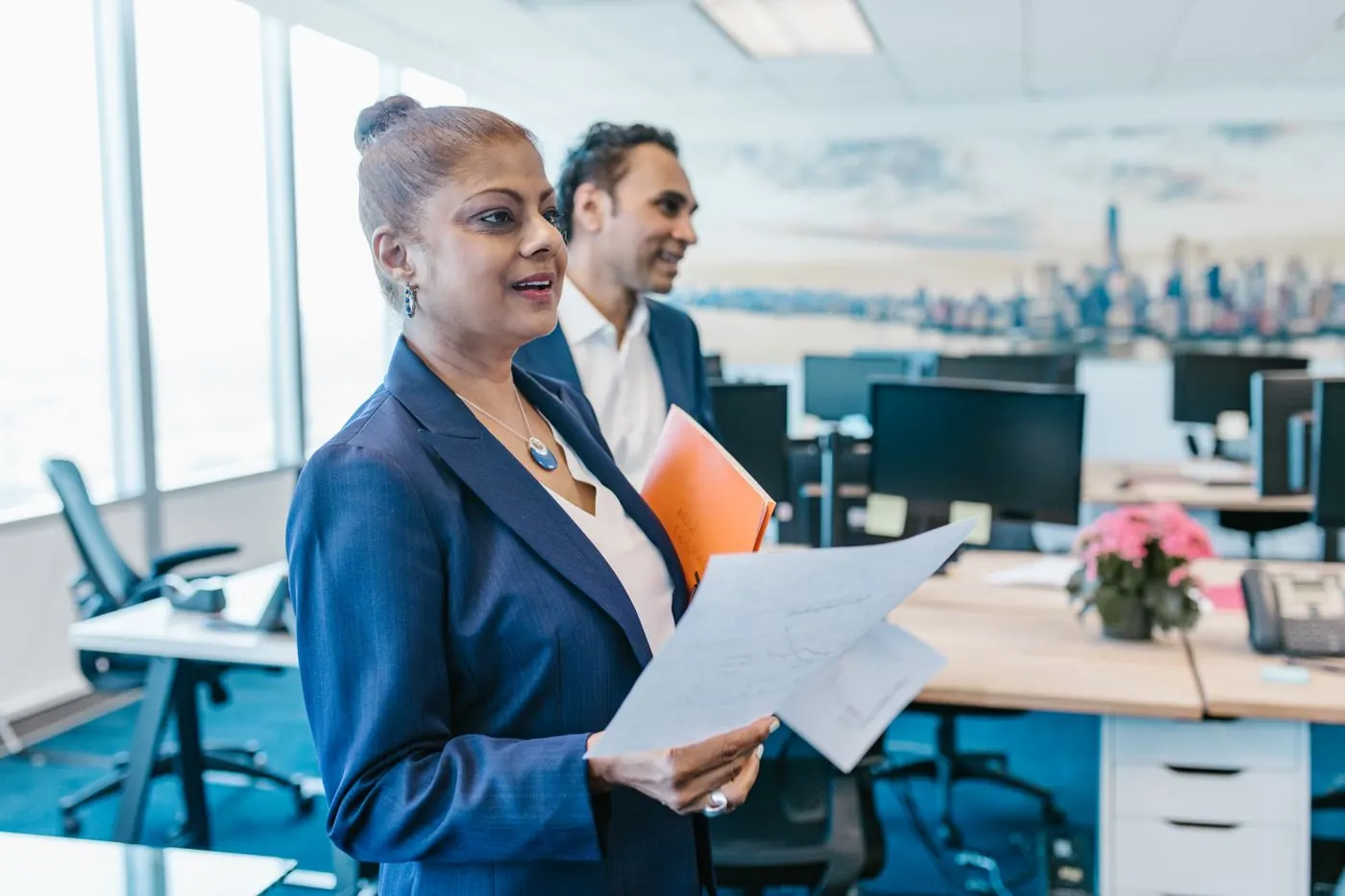A manager walking through her office, papers in hand, smiling